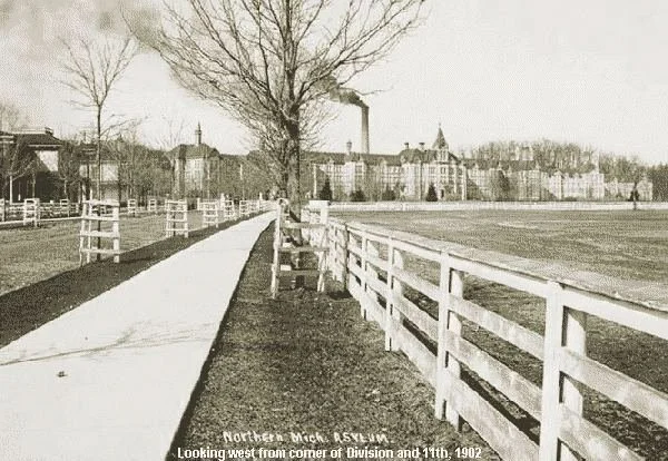 Historic photograph of Building 50 at the Traverse City State Hospital, with a wooden fence in the foreground.