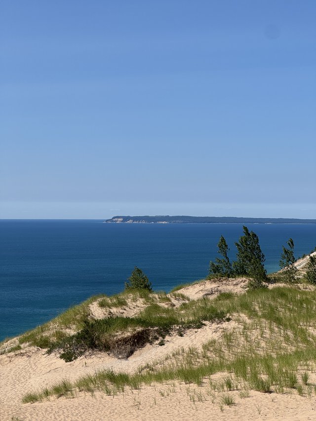 Dune grass and sand above deep blue Lake Michigan, with one of the Manitou Islands low on the horizon.